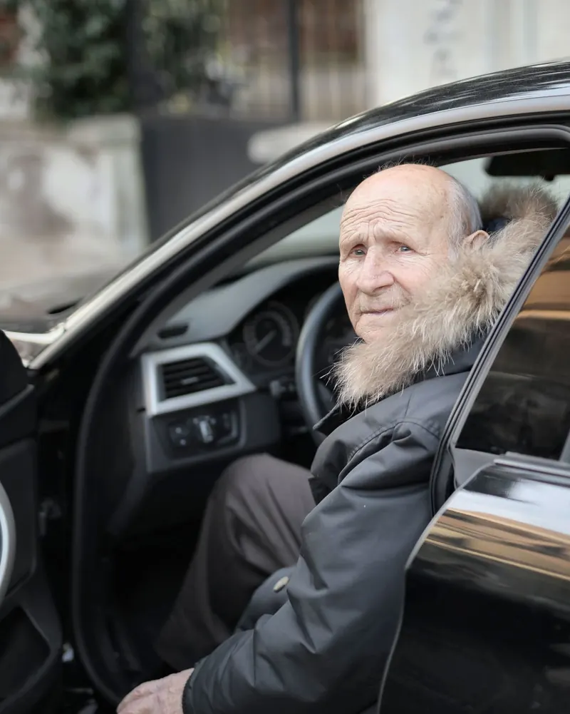 Älterer Fahrgast steigt lächelnd aus einem Auto